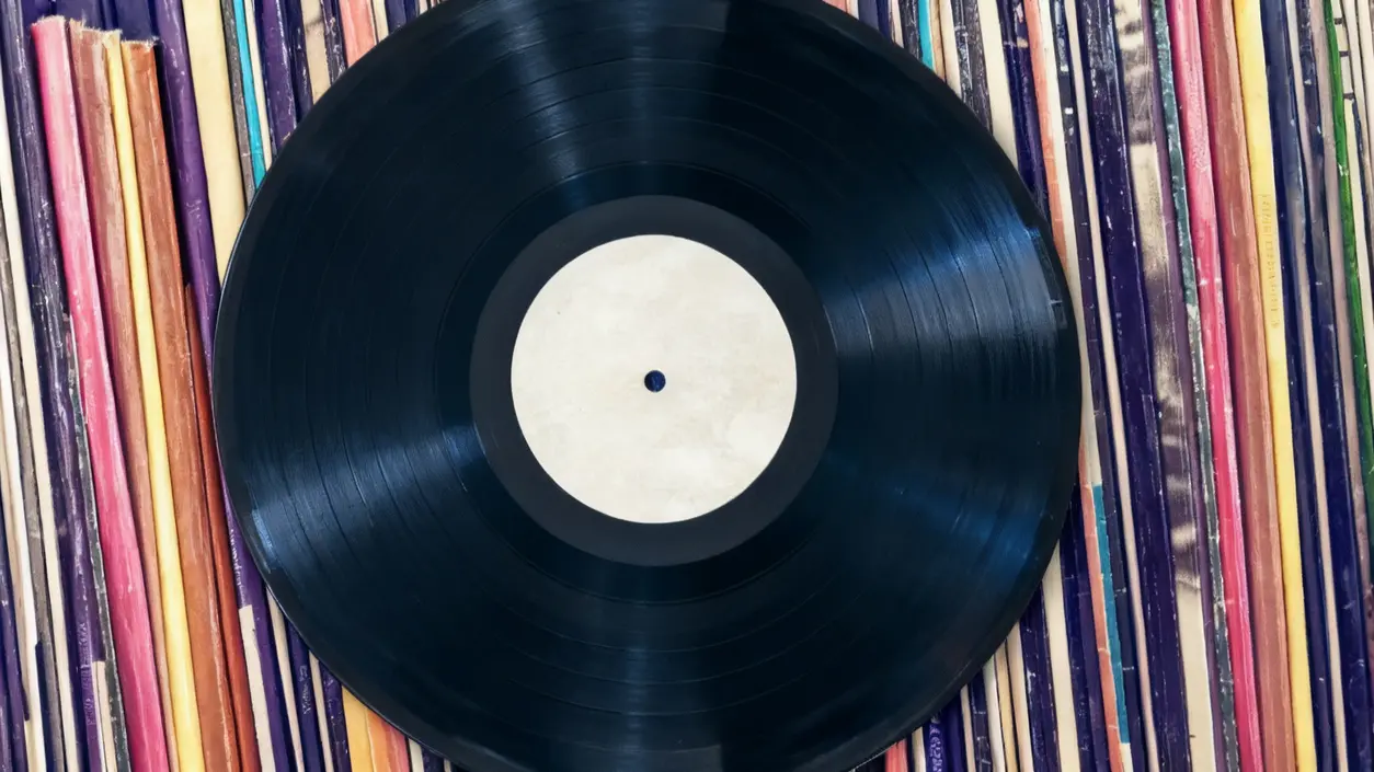 Un disco in vinile nero su una collezione di copertine colorate di altri dischi