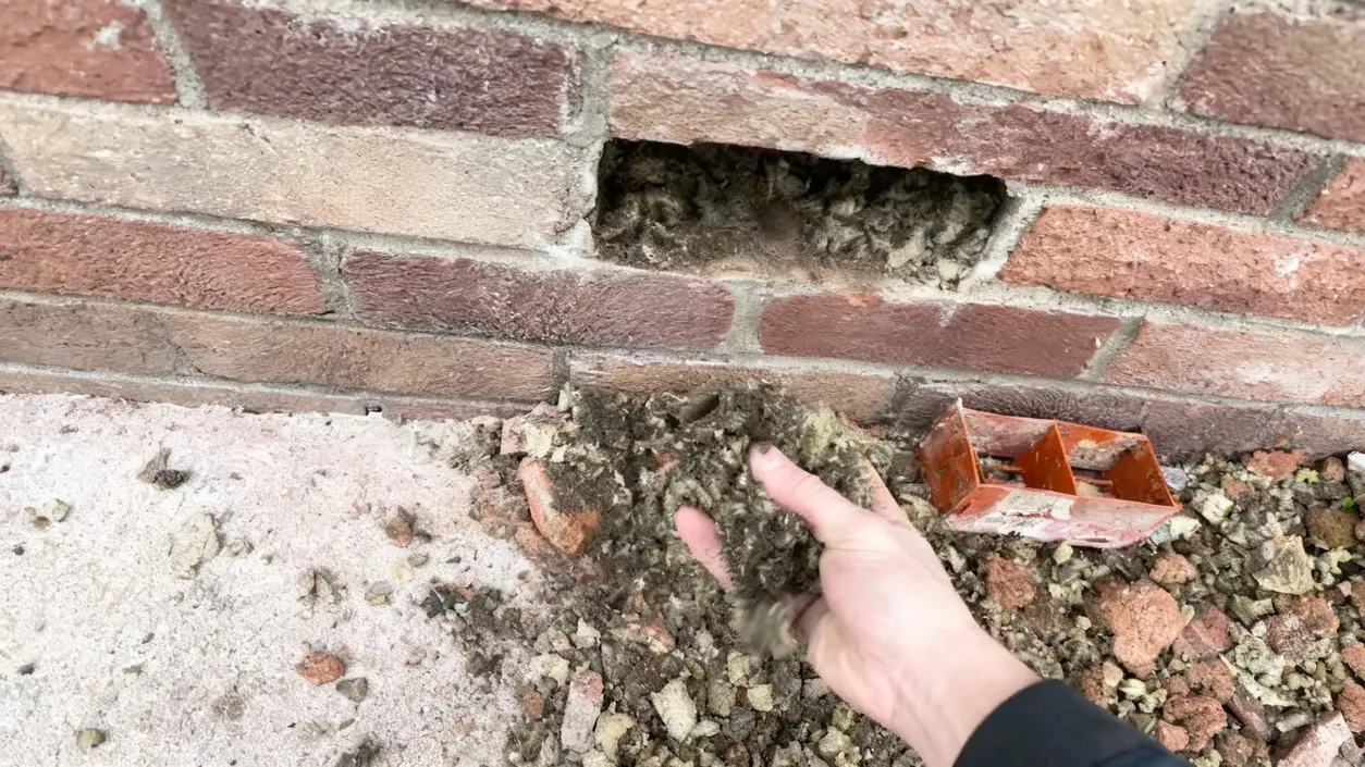 Mano che rimuove vecchio isolamento da un foro in un muro in mattoni