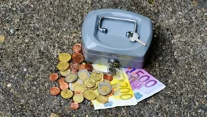 Una piccola cassetta di sicurezza con chiave accanto a monete e banconote sparse su una superficie ruvida