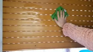 Persona che pulisce una tapparella marrone con un panno verde