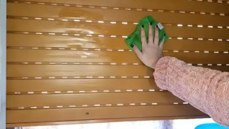 Persona che pulisce una tapparella marrone con un panno verde