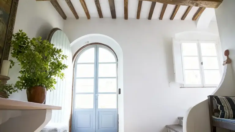 Ingresso luminoso con porta ad arco, pianta verde e soffitto con travi a vista