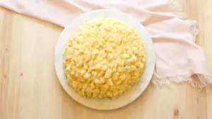 Torta mimosa soffice su piatto bianco, vista dall'alto su tavolo di legno chiaro