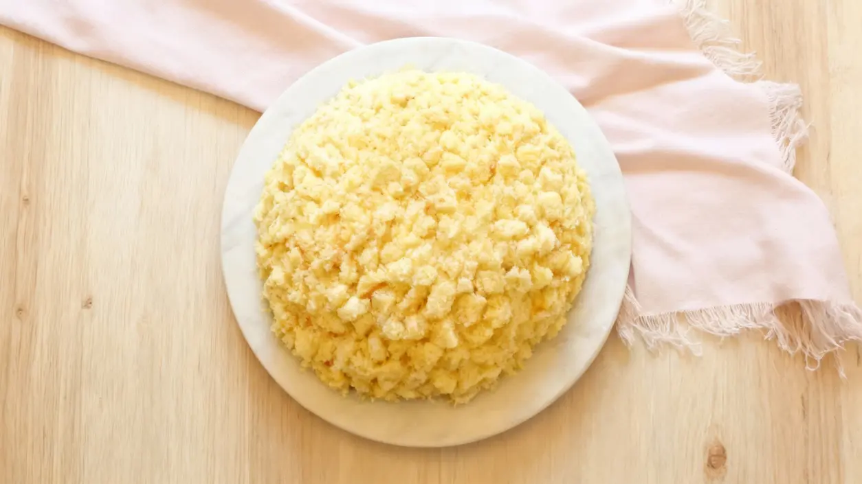 Torta mimosa soffice su piatto bianco, vista dall'alto su tavolo di legno chiaro