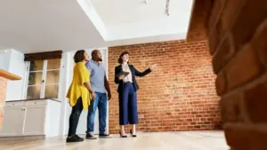 Tre persone osservano l'interno di un appartamento con pareti in mattoni a vista