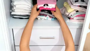 Persona che sistema magliette piegate in un cassetto di un armadio bianco.