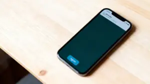 Smartphone con schermata di WhatsApp aperta su un tavolo in legno chiaro