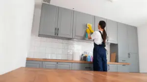 Persona che pulisce i pensili della cucina con un panno e spray detergente